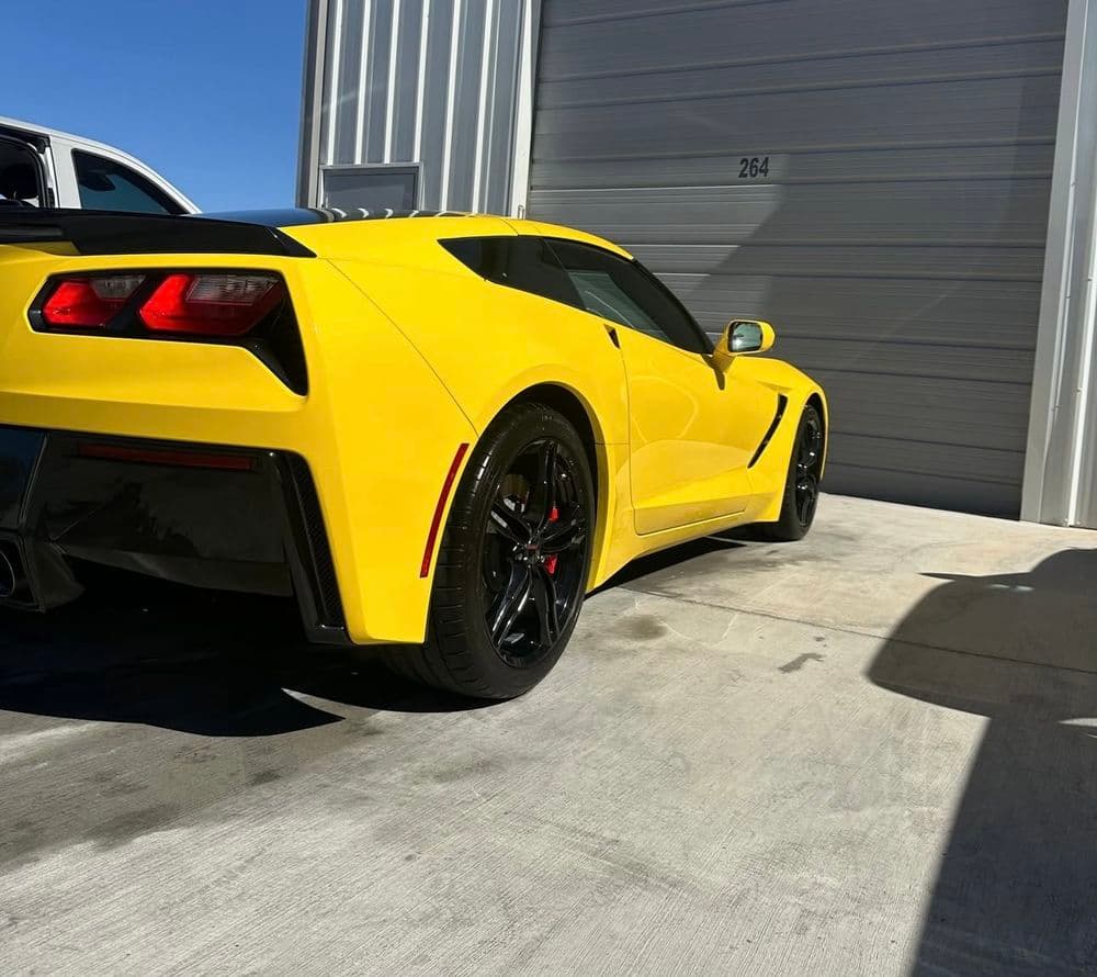 Yellow sports car parked outside a garage, showcasing its sleek design and black accents.