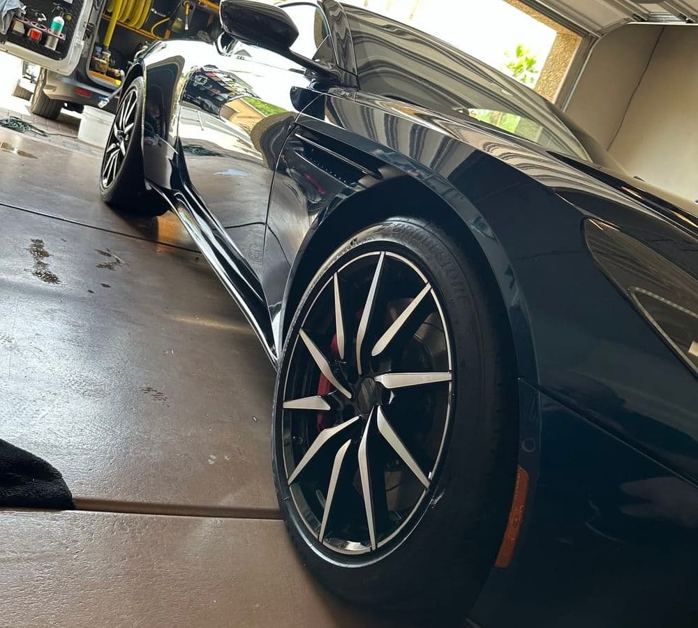 Sleek black sports car with shiny wheels parked in a garage.