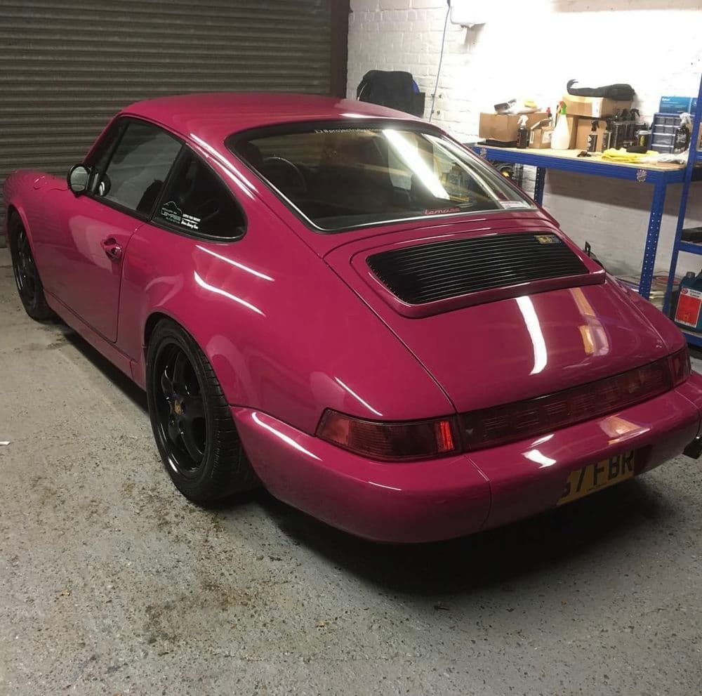 Pink Porsche 911 in a garage with black wheels and tools in the background.