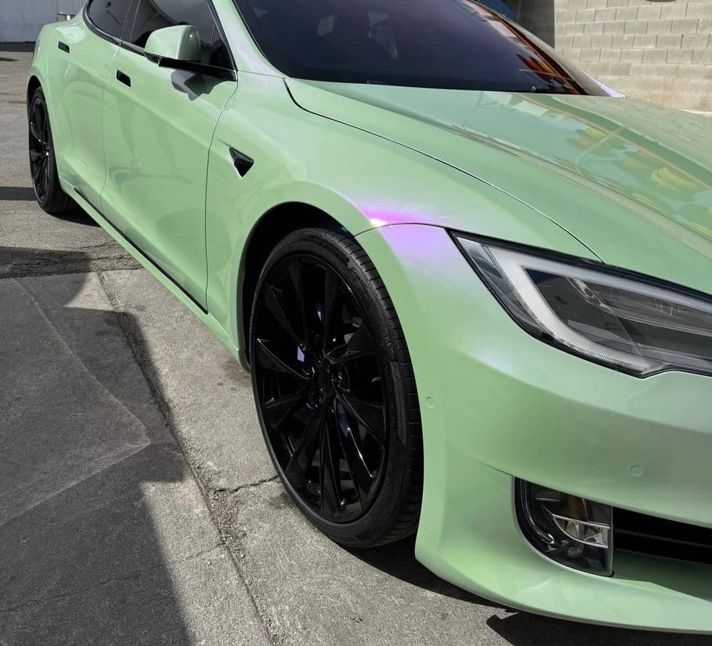 Mint green Tesla Model S with black wheels parked on a concrete surface.