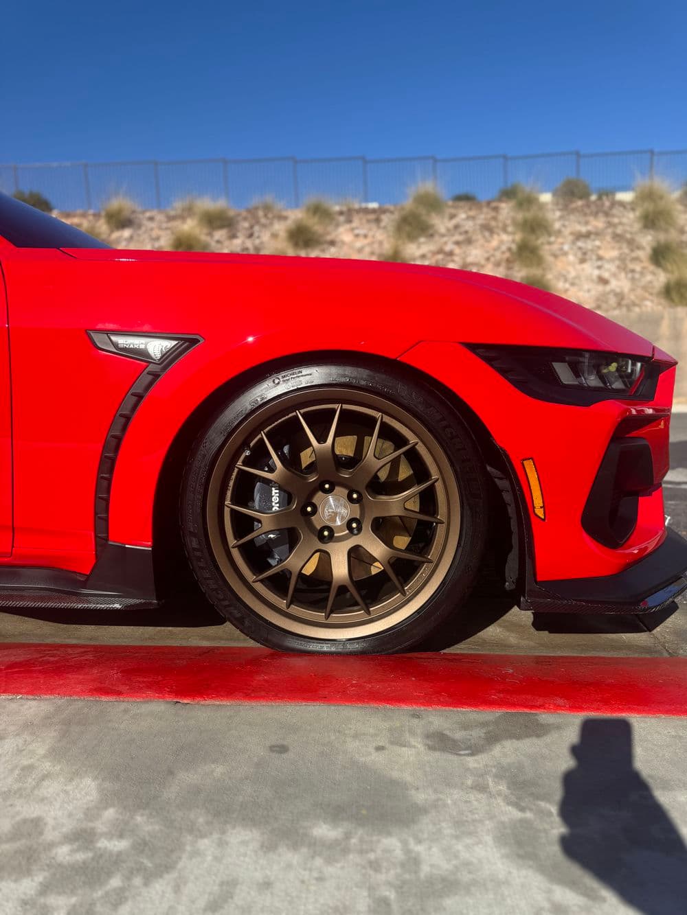 Red sports car with bronze wheels and detailed tire showcased on a racetrack.